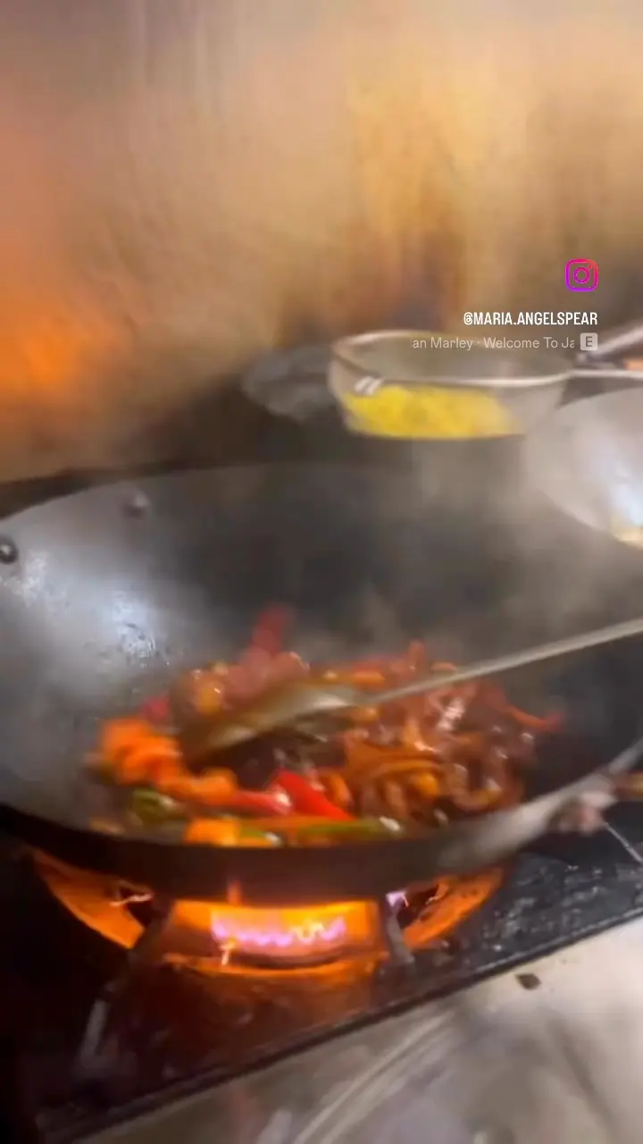 A wok of vegetables and chicken cooking over an open flame at Nice and Knuff